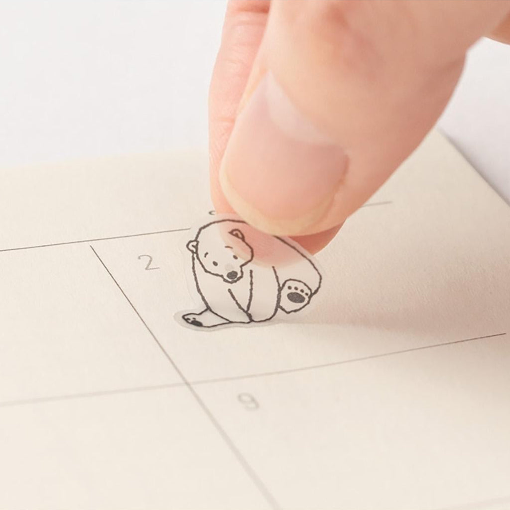 Small bear-shaped sticker on a planner page with a hand pressing it down.