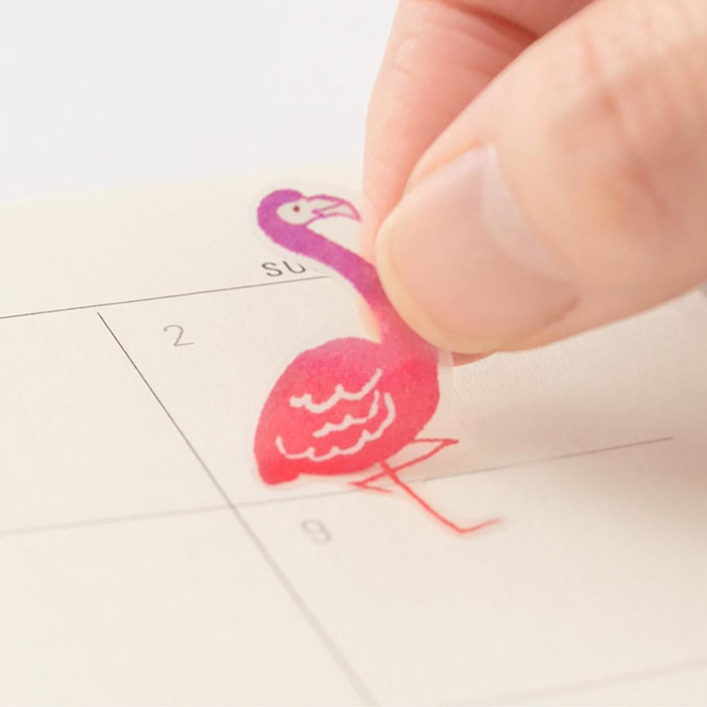 Hand applying a pink flamingo-shaped sticker to a calendar.