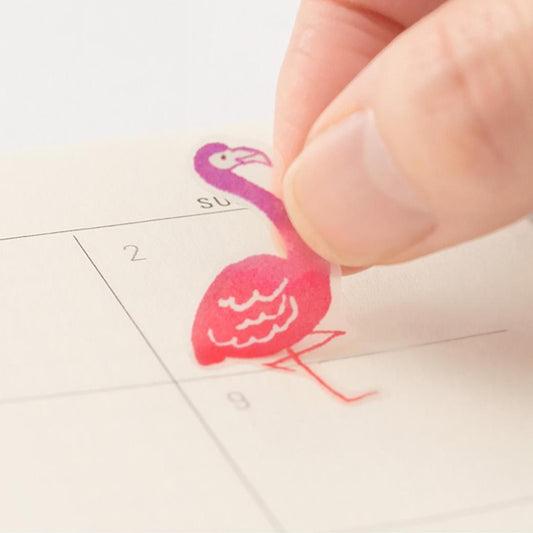 Hand applying a pink flamingo-shaped sticker to a calendar.