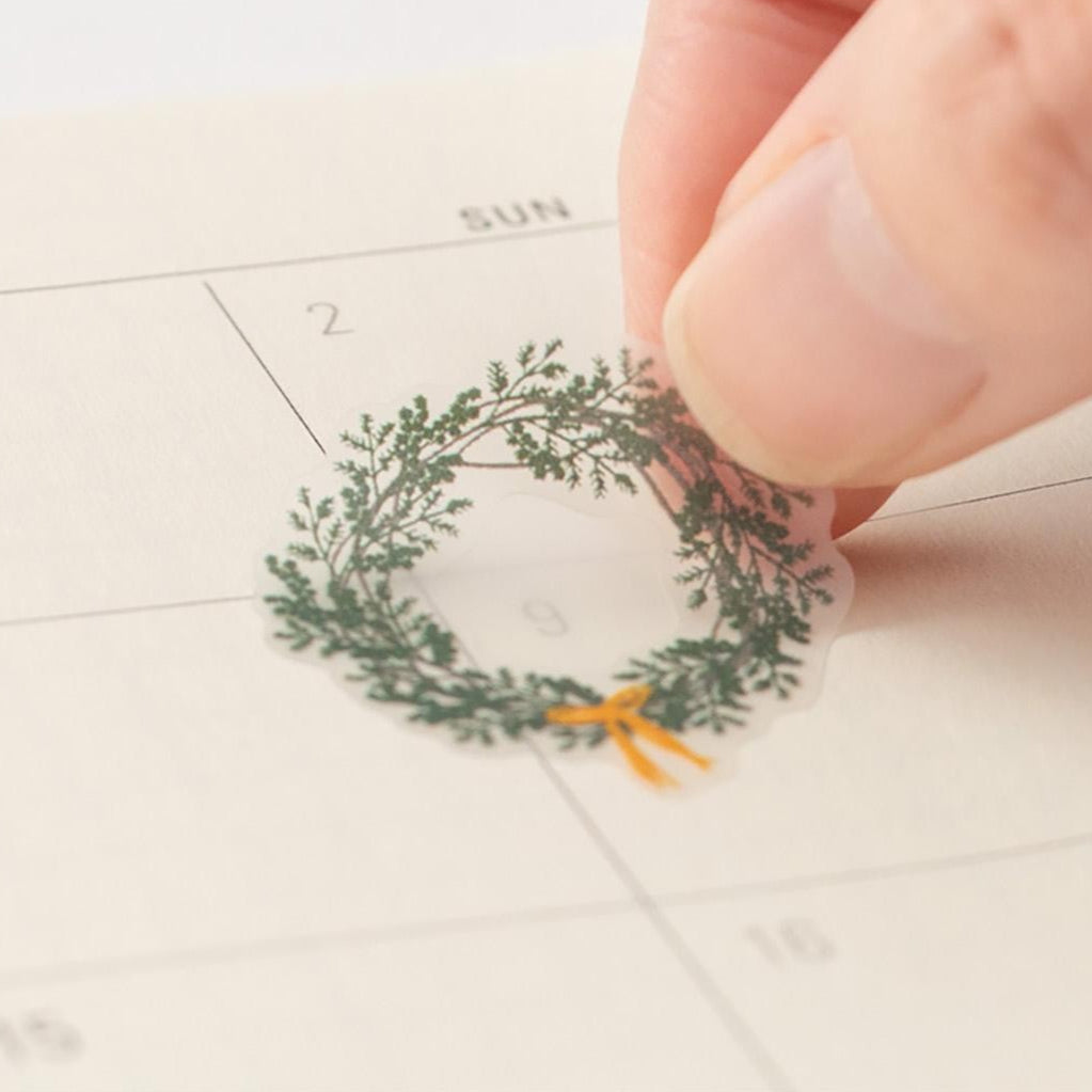 Small decorative wreath with a bow being placed on a calendar.