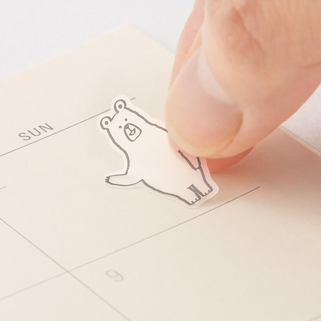 Hand placing a small white bear-shaped sticker on a calendar.