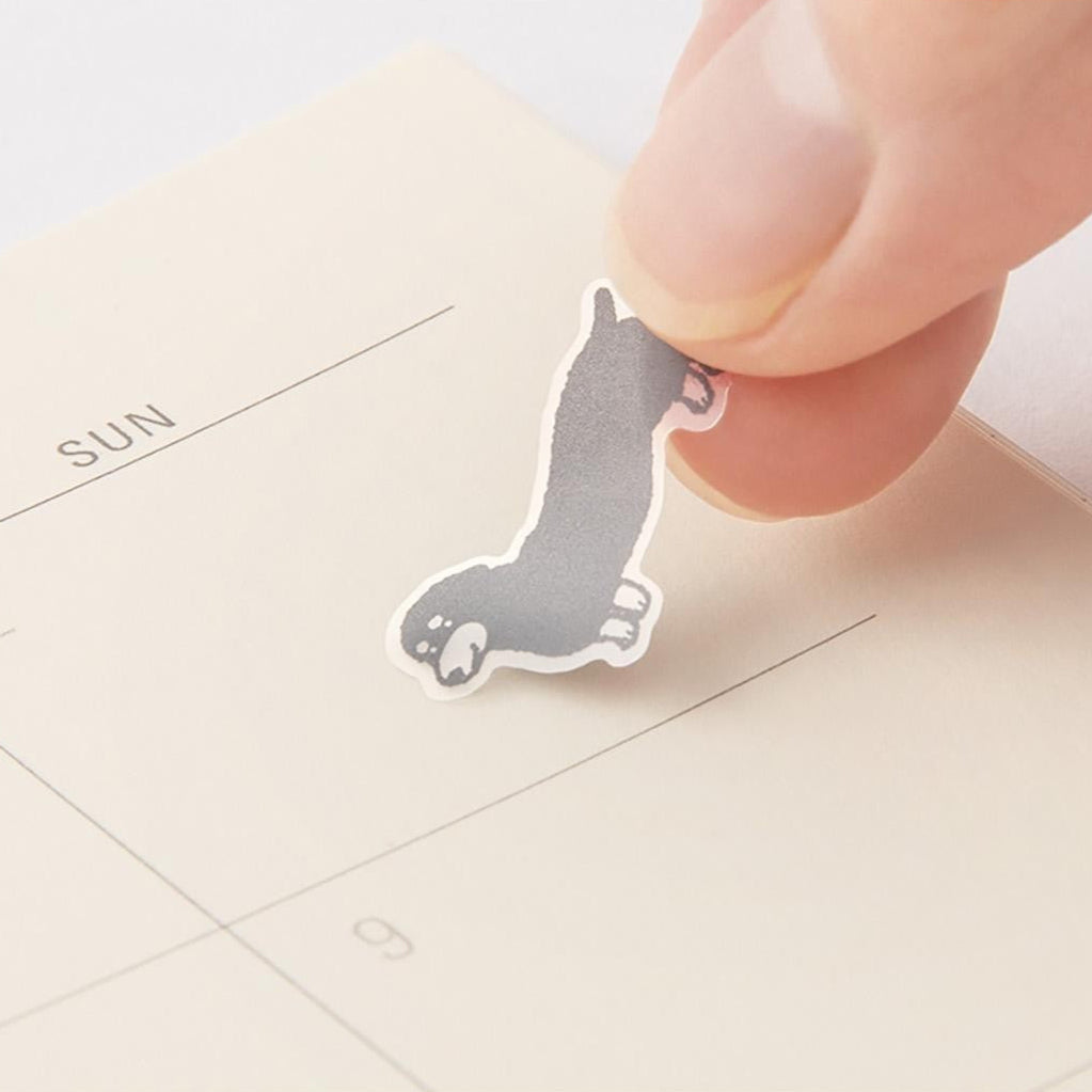Hand holding a small dog-shaped sticker over a calendar