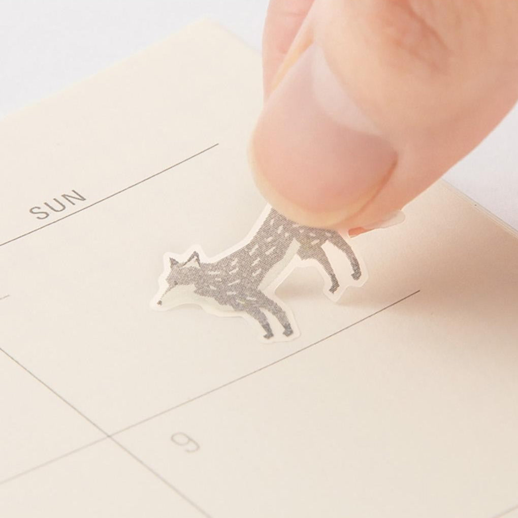 Small wolf seal sticker being pressed onto a calendar sheet with a hand visible.