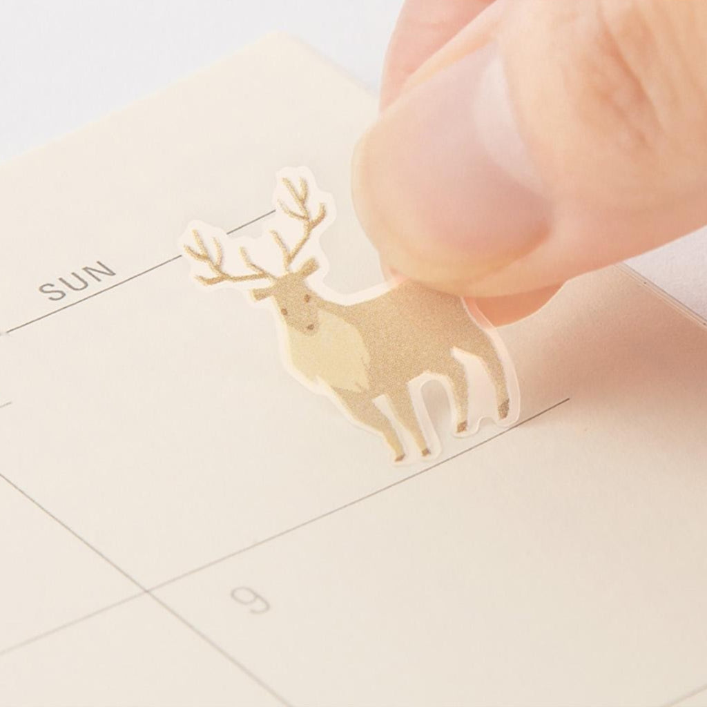 Hand holding a small deer-shaped seal sticker over a calendar