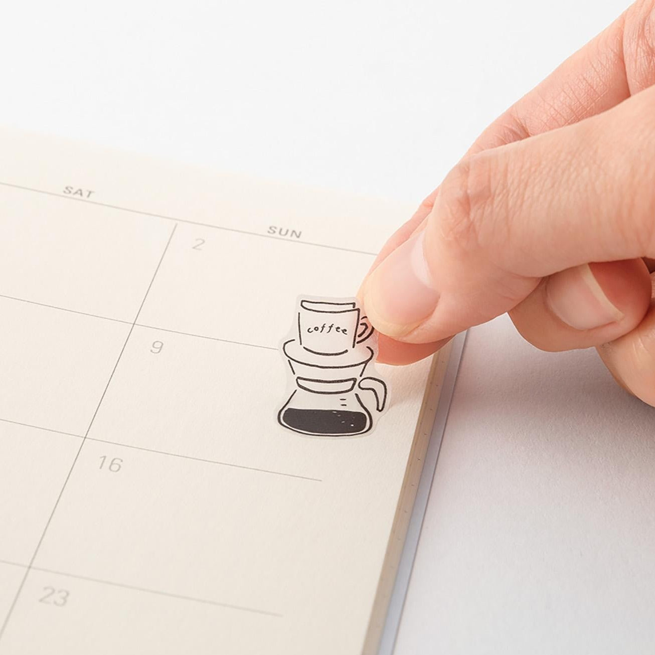Hand applying a coffee-themed sticker to a planner page.