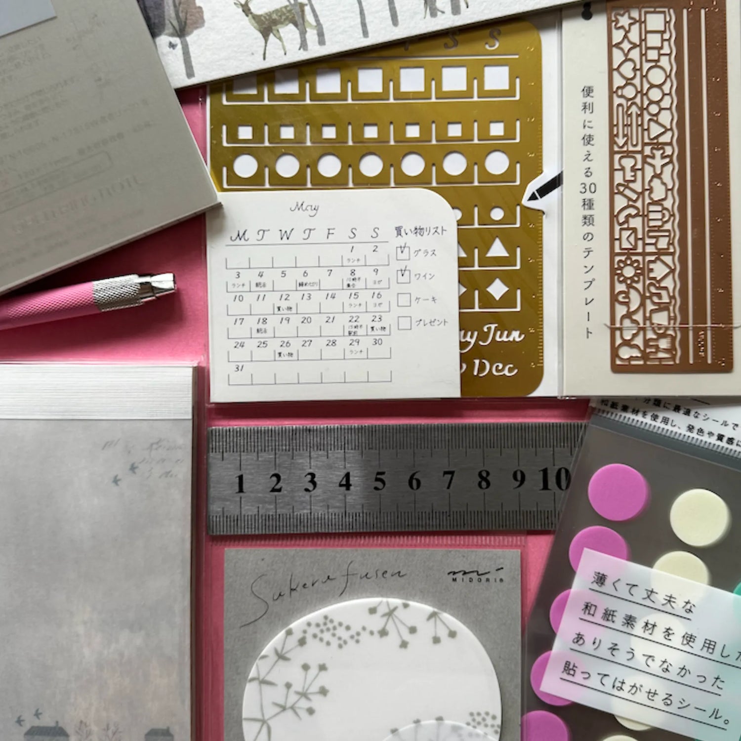 Japanese stationery tools including stencils, sticky notes, rulers, and paper accessories on a pink background