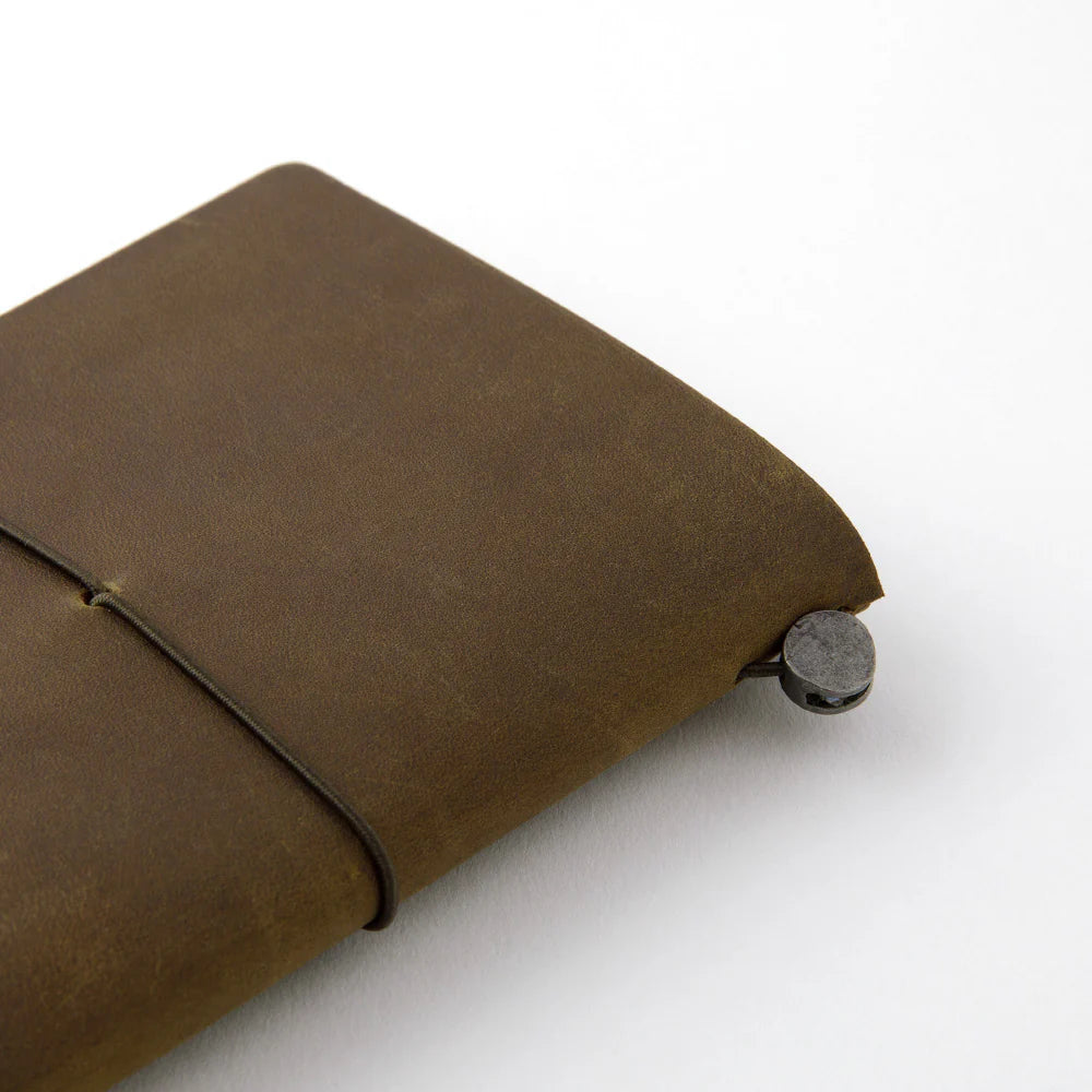 TRAVELER’S notebook in Olive – a dark brownish-green leather cover with earthy, rugged tones that deepen and develop a rich patina over time. Includes cotton bag, blank refill, and spare band.
