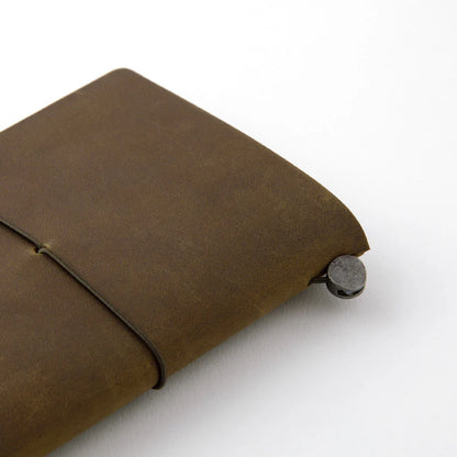 TRAVELER’S notebook in Olive – a dark brownish-green leather cover with earthy, rugged tones that deepen and develop a rich patina over time. Includes cotton bag, blank refill, and spare band.