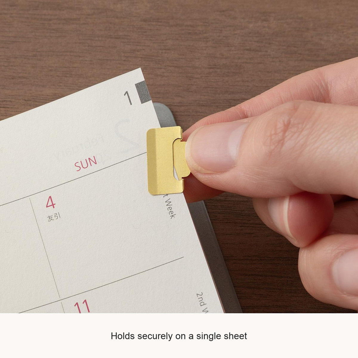 Hand attaching a Midori Chiratto small brass index clip to a page, with English feature captions