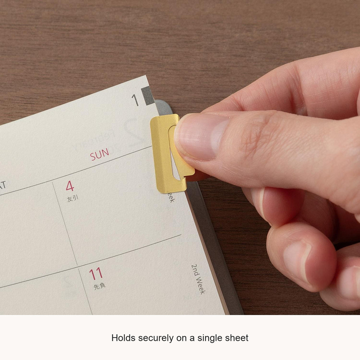 Hand attaching a Midori Chiratto medium brass index clip to a page, with English feature captions