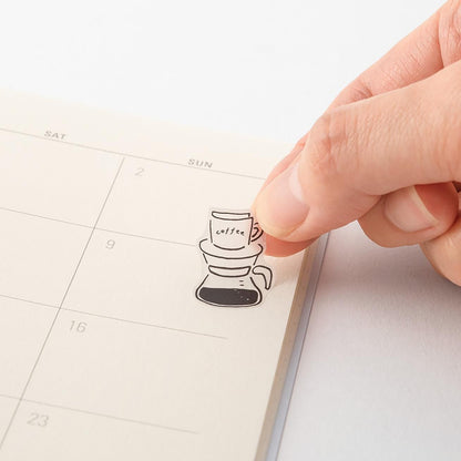 Hand applying a coffee-themed sticker to a planner page.