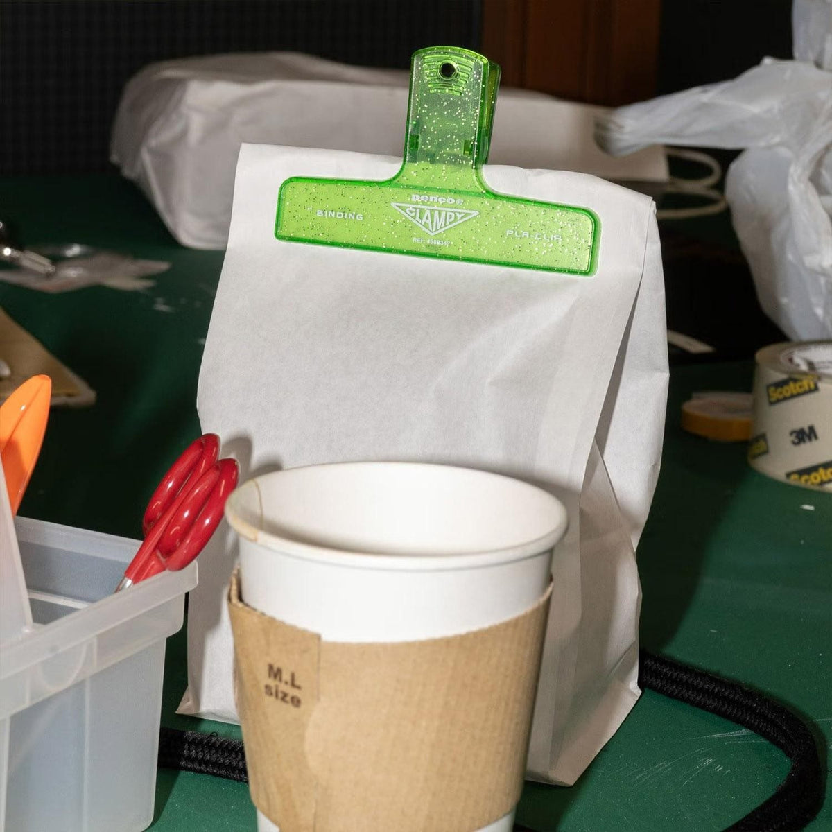Green glitter Penco Clampy clip sealing a paper bag beside a takeaway cup