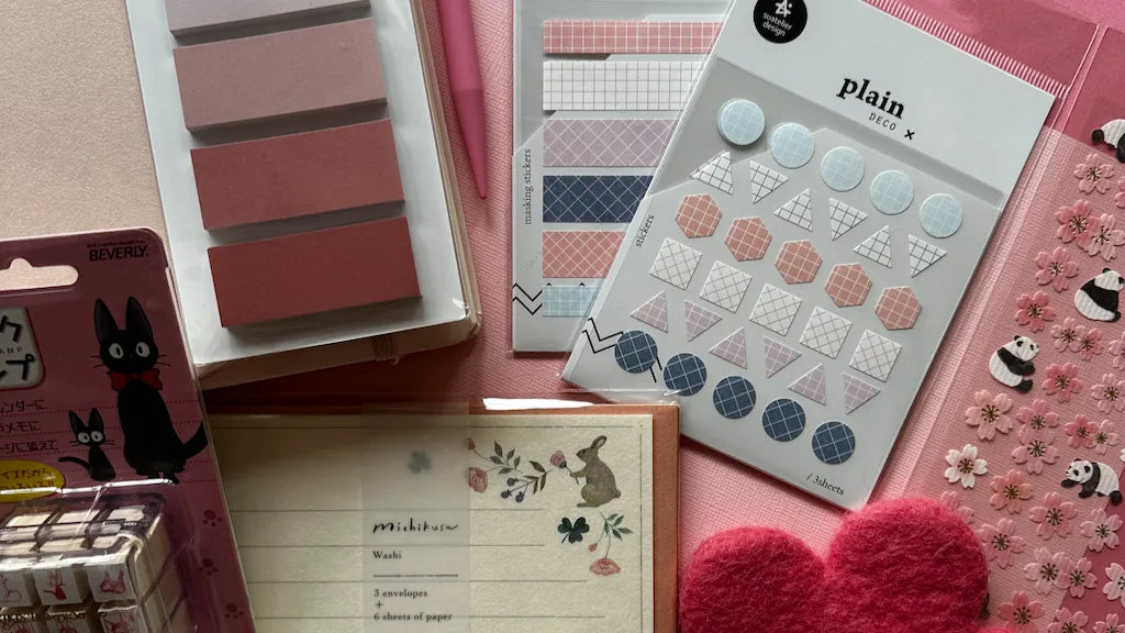 Aesthetic flatlay of Korean and Japanese stationery including pastel sticky notes, geometric planner stickers from Suatelier and Midori, panda and cherry blossom 3D stickers, Beverly cat rubber stamps, and floral washi envelopes on a pink background